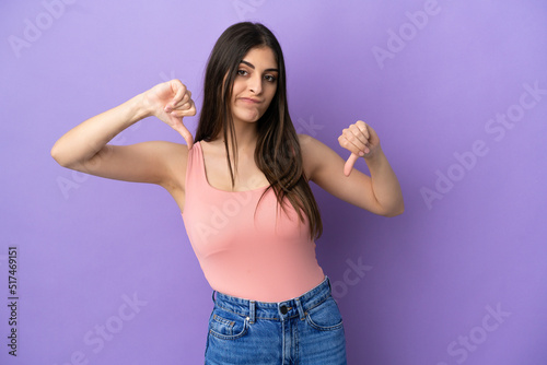 Young caucasian woman isolated on purple background showing thumb down with two hands