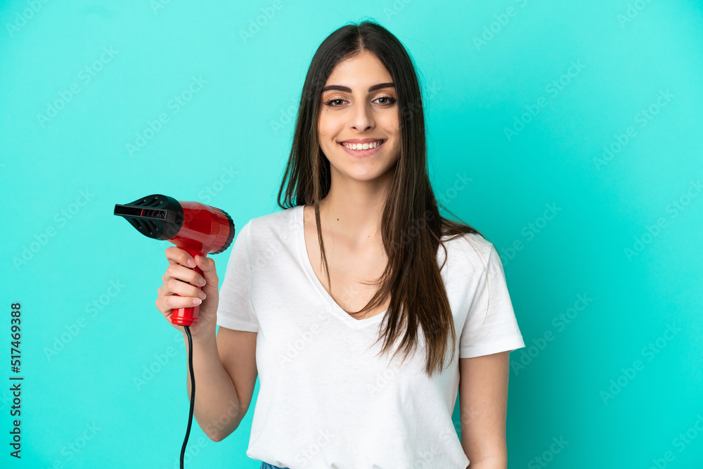Young caucasian woman holding a hairdryer isolated on blue background smiling a lot Young caucasian woman holding a hairdryer isolated on blue background smiling a lot