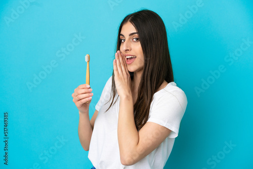 Young caucasian woman brushing teeth isolated on blue background whispering something