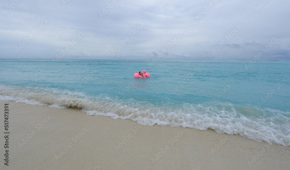 girl floats on an inflatable pink flamingo in the ocean