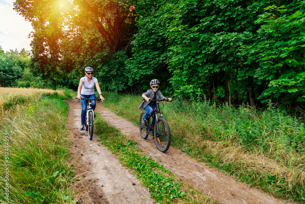 Naklejka premium mather and her son cycling in summer in the park on bicycles