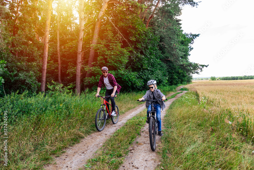 Naklejka premium father and his son cycling in summer in the park on bicycles