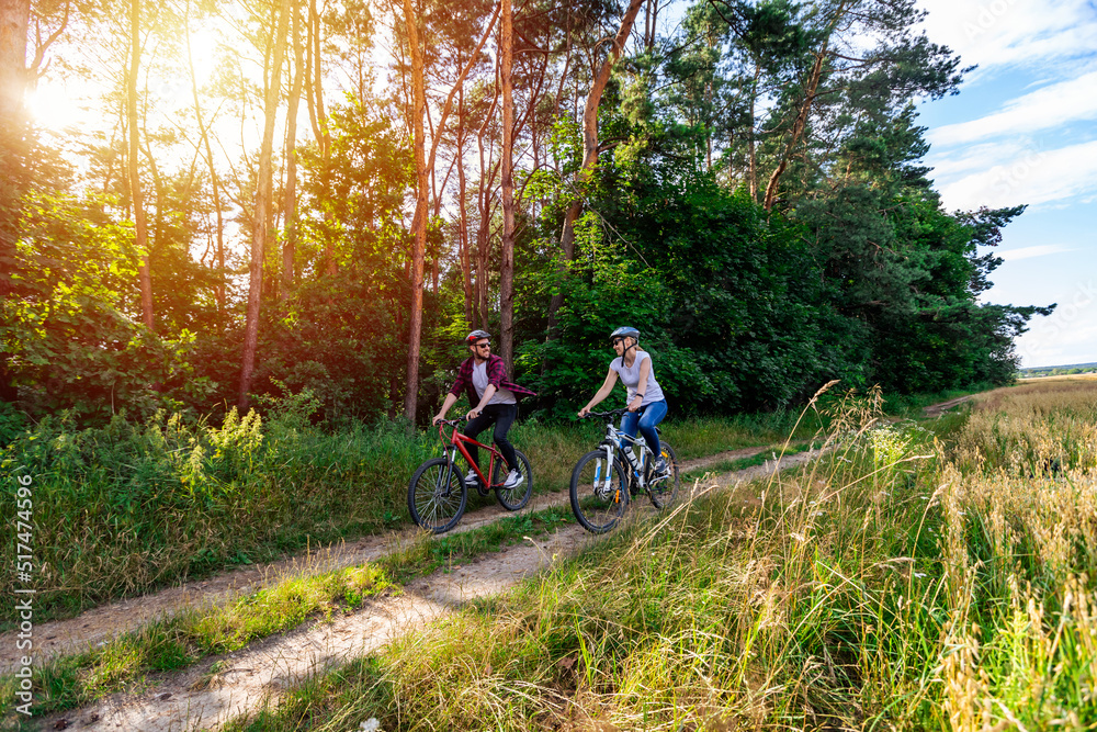 Naklejka premium woman and a man cycling in summer in the park on bicycles