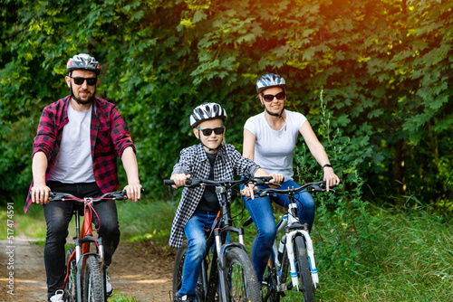 Cheerful young family cycling in summer in the park on bicycles