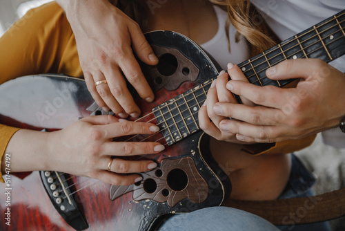 Close-up of the hands of a man and a woman holding a guitar