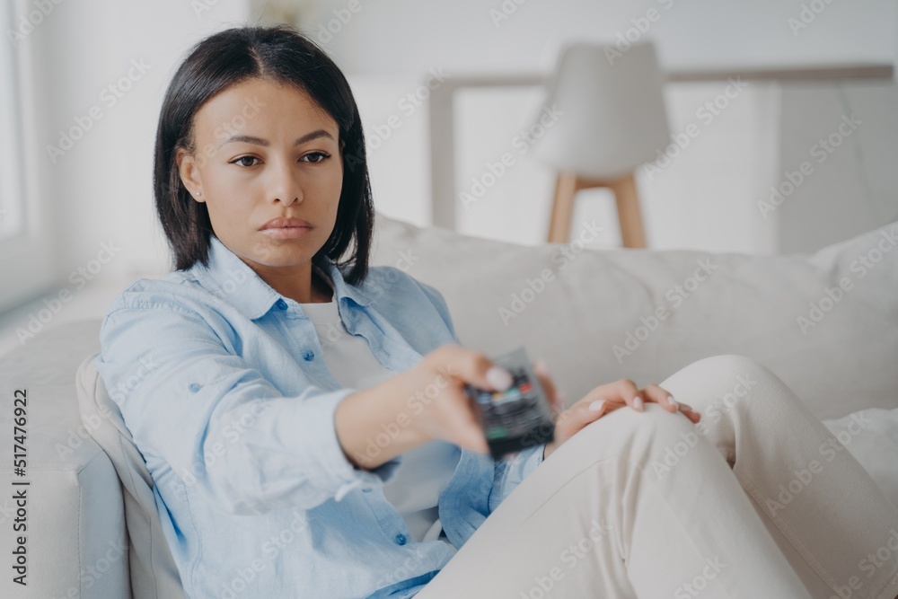 Bored female holding tv remote control change channels, watching television sitting on couch at home