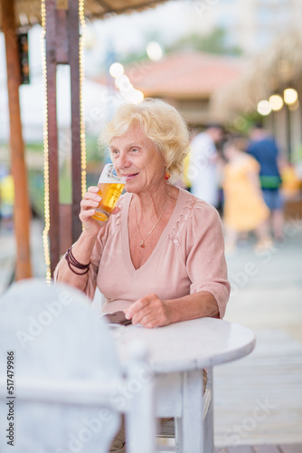 Senior woman sitting at a table in a summer cafe and drinking beer from a tall glass