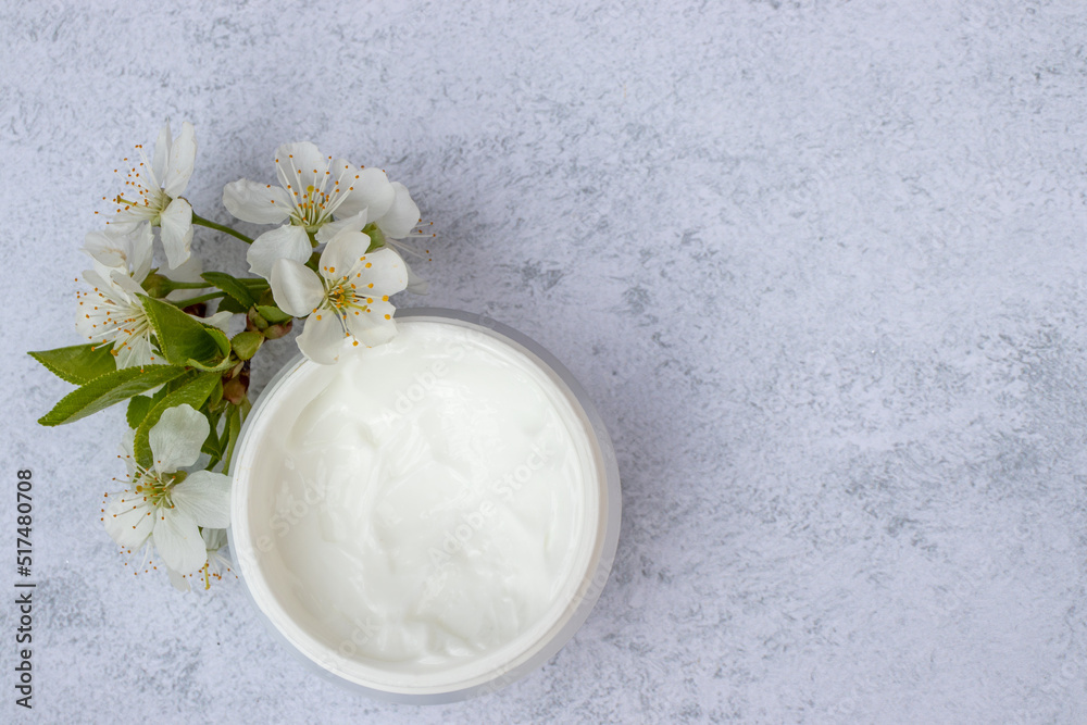 Cosmetic facial body cream in glass jar and flowers on marble table. Minimalists still life with beauty products and white flowers on white background. Flat lay, top view, copy space Cosmetic facial body cream in glass jar and flowers on marble table. Minimalists still life with beauty products and white flowers on white background. Flat lay, top view, copy space