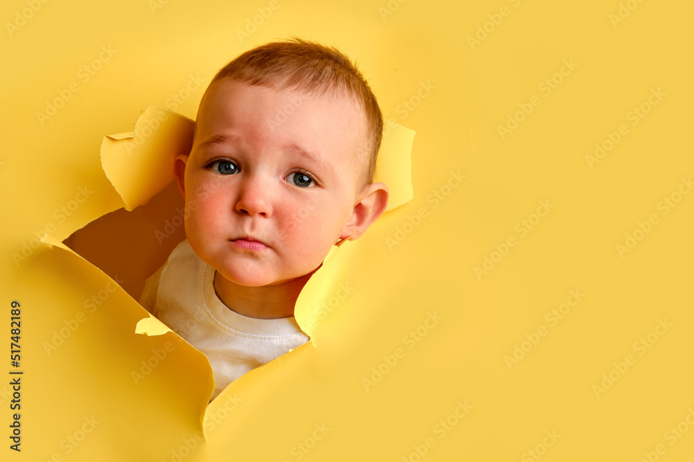Sad child looks out of a hole in the studio yellow background. Cry baby ...