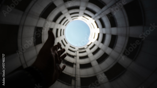 A person stretches there hand in the air towards the sky in a spiral entrance tube of a concrete parking garage. Wide angle shot from bottom to top