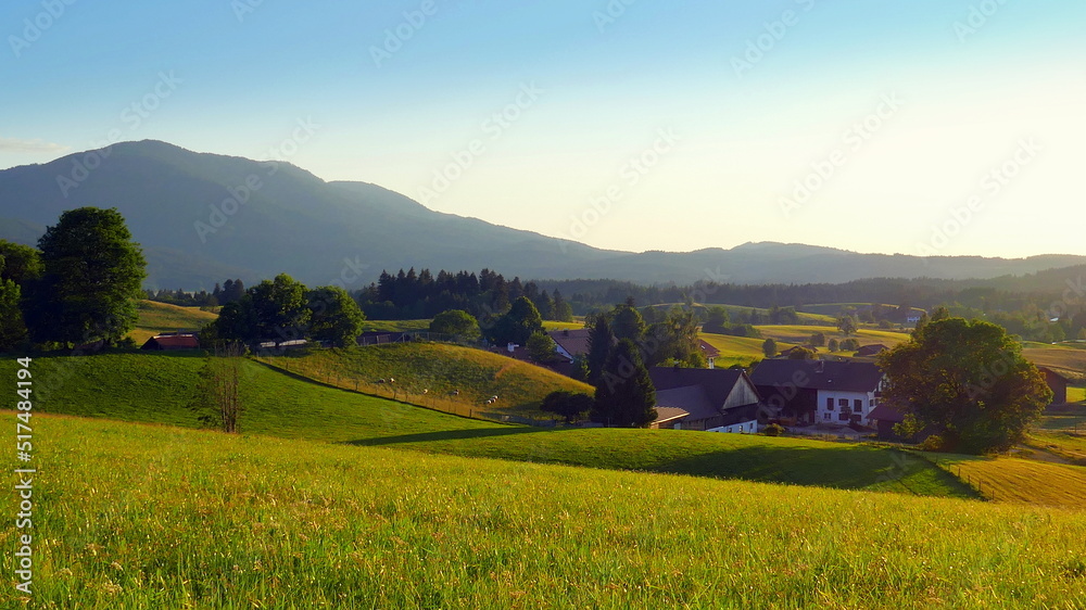 malerische Blick auf Wiesen, Berge und Bauernhof im warmen Abendlicht in Bayern unter blauem Himmel