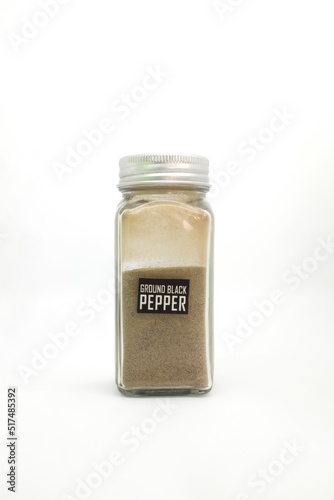 Ground black pepper powder in spice condiment glass bottle with label isolated in white background.
