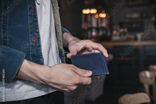 A young man stands in a cafe and holds a blue leather wallet in his hands. Lifestyle. Close-up, no face, horizontal orientation, copy space