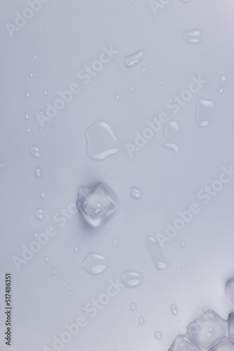Ice cubes and water drops scattered on white background