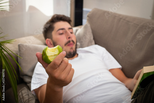 Fotografia un jeune homme allongé sur un canapé se relaxe en mangeant une pomme et en lisan