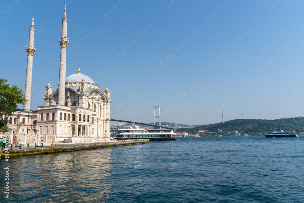 Ortakoy Mosque, with the Bosphorus to the side, and the bridge that crosses it in the background of the image, with the afternoon sun on a sunny day.