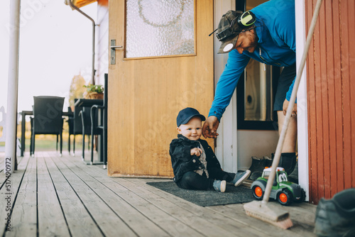 Smiling father playing with son sitting on doormat at porch photo