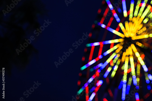Blurred view of beautiful glowing Ferris wheel against dark sky. Space for text