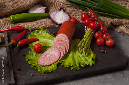 smoked servelat on a wooden board decorated with fresh vegetables photo