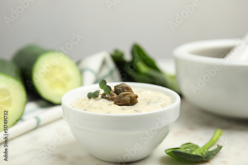 Creamy caper sauce in bowl on white marble table, closeup