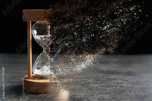 Time is running out. Hourglass vanishing on grey table against black background © New Africa