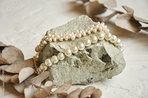White pearl necklace on a stone with eucalyptus leaves. Photo toned, selective focus
