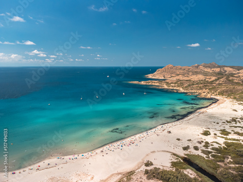 Aerial view of holidaymakers enjoying the sunshine and turquoise Mediterranean sea in the Balagne region of Corsica with the rocky coast of Desert des Agriates behind