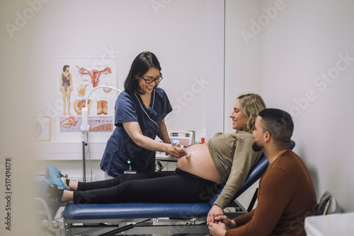 Smiling gynecologist doing ultrasound of pregnant woman sitting by man at hospital photo