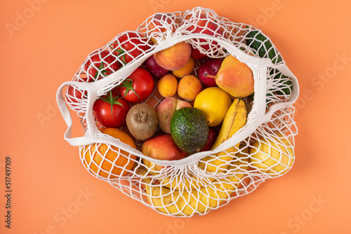 Reusable string bag with organic fruits and vegetables on orange background. Top view. Healthy diet food. Flat lay