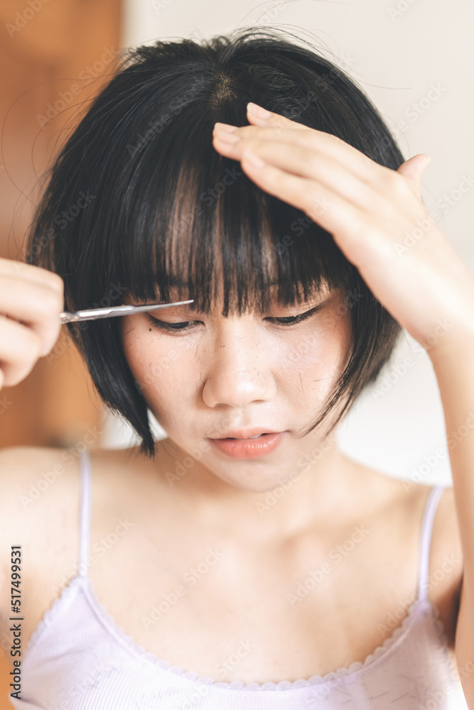 Fototapeta premium Young adult authentic asian woman self cutting bangs haircut with scissors