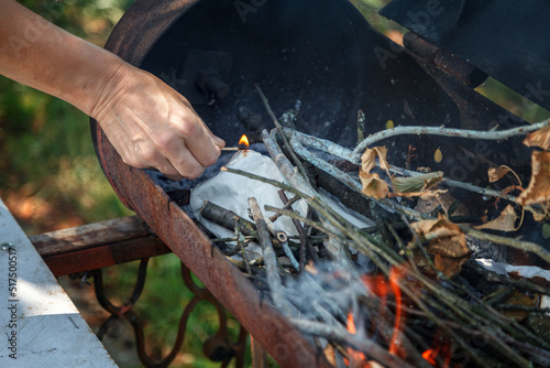 A womans hand burns paper in a barbecue with a burning match