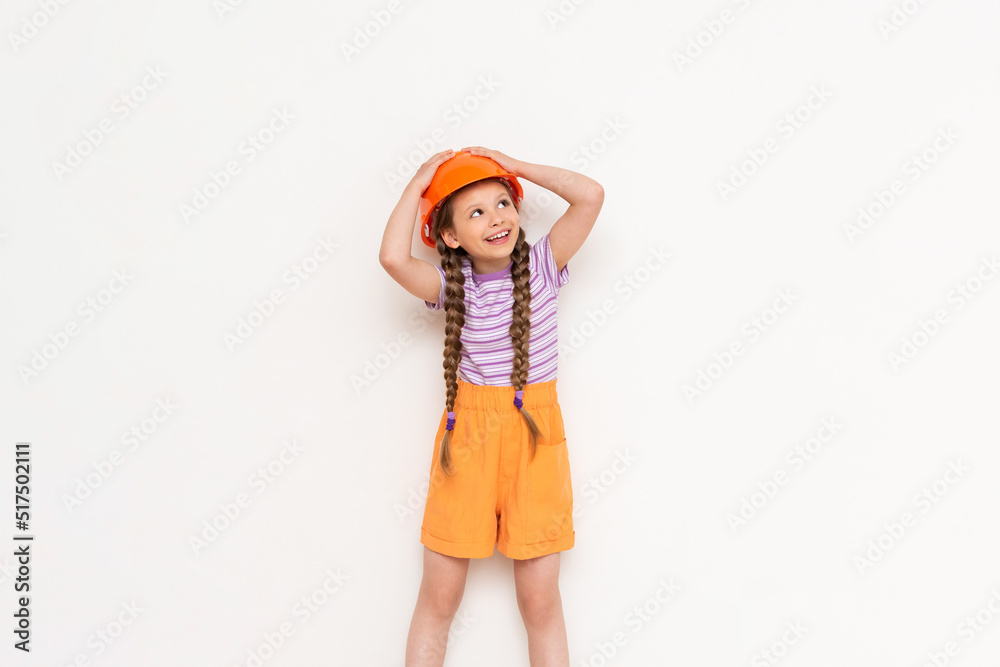 A child in a construction helmet holds his head with his hands. A beautiful little girl is getting ready for repairs on a white isolated background. A child in a construction helmet holds his head with his hands. A beautiful little girl is getting ready for repairs on a white isolated background.