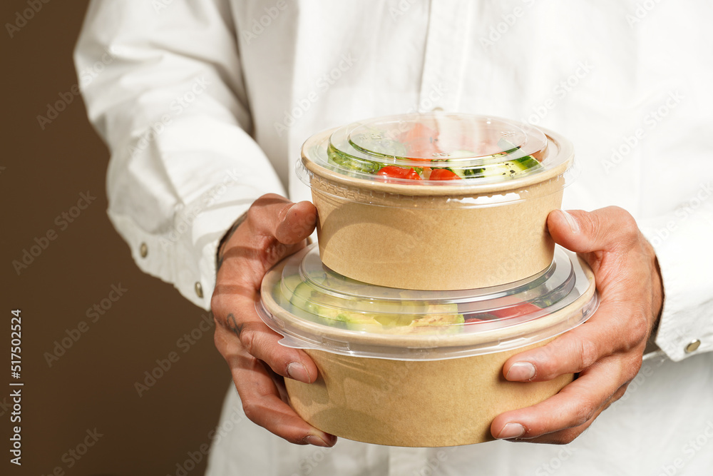 Man in white shirt holding Trendy dish poke bowl - rice, wakame seaweed, tomatoes, cucumber, avocado, salmon in recycled round carton with sustainable fork, takeaway food concept Man in white shirt holding Trendy dish poke bowl - rice, wakame seaweed, tomatoes, cucumber, avocado, salmon in recycled round carton with sustainable fork, takeaway food concept