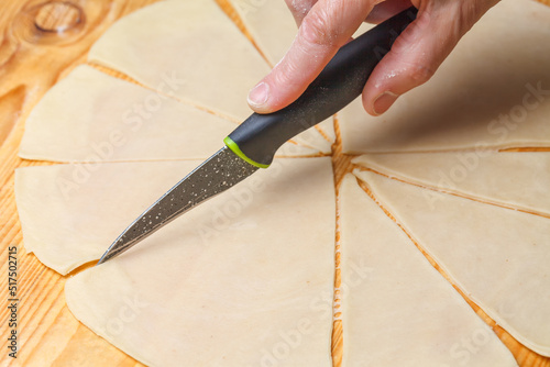 A womans hand cuts the dough with a kitchen knife
