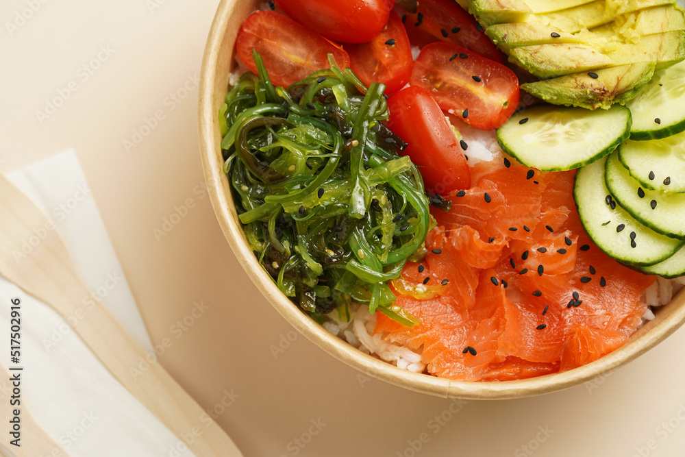 Trendy wholesome dish poke or buddha bowl - rice, wakame seaweed, tomatoes, cucumber, and red fish salmon - in a recycled round carton with sustainable fork, takeaway food concept on beige background Trendy wholesome dish poke or buddha bowl - rice, wakame seaweed, tomatoes, cucumber, and red fish salmon - in a recycled round carton with sustainable fork, takeaway food concept on beige background