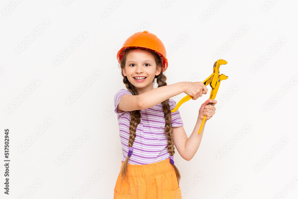 A little girl in an orange construction helmet holds a wrench on a white isolated background. The concept of renovation in the children's room. A little girl in an orange construction helmet holds a wrench on a white isolated background. The concept of renovation in the children's room.