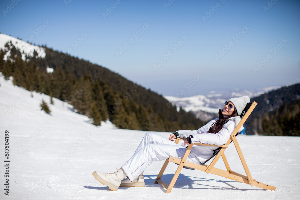 Young woman sitting at deck chair on ski track at the snowy mountain