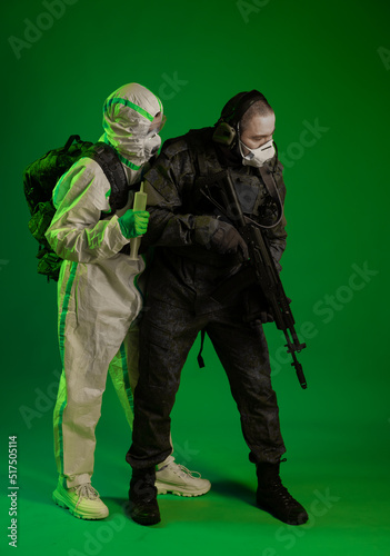 soldier in the studio on a green background with a medic or scientist in a white protective suit. a man in military uniform with a rifle or a machine gun, a man in chemical protection