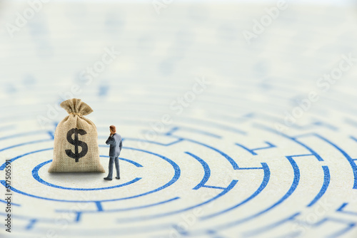 Reducing or overcome financial barrier, financial concept : US dollar bag on a maze puzzle with a businessman considers how to overcome financial difficulties. CFO wishes to avoid a financial crisis.