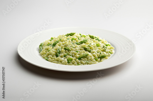 White flat plate of risotto with green asparagus