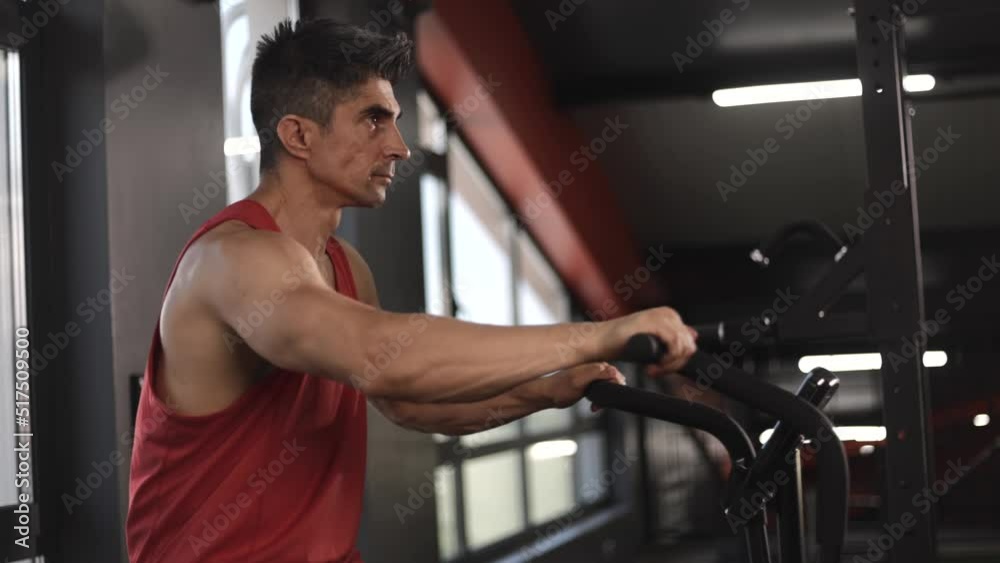 Shot of mature man sitting on stationary bicycle or exercise bike in gym. Caucasian muscle man spinning on cardio machine. Health care and fitness in gym concept.
