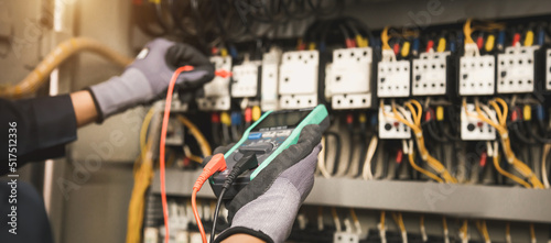 Electricity and electrical maintenance service, Engineer hand holding AC multimeter checking electric current voltage at circuit breaker terminal and cable wiring main power distribution board.