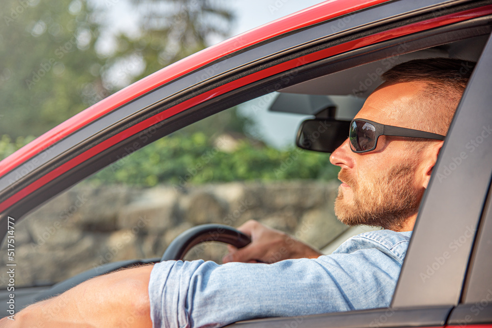 A man with a smile on his face drives a red car.