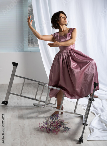 portrait of a graceful girl in a pink dress in the studio, a beautiful woman with black hair is dancing with a bouquet of flowers around the stairs, stepladder. White background.