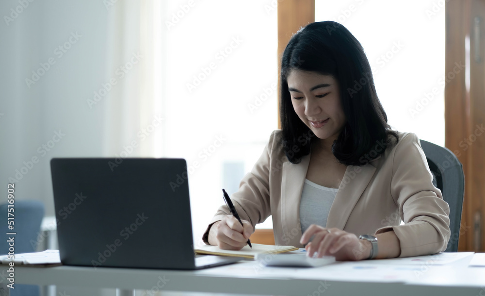Beautiful Asian businesswoman analyzes charts using laptop calculator at the office. Beautiful Asian businesswoman analyzes charts using laptop calculator at the office.