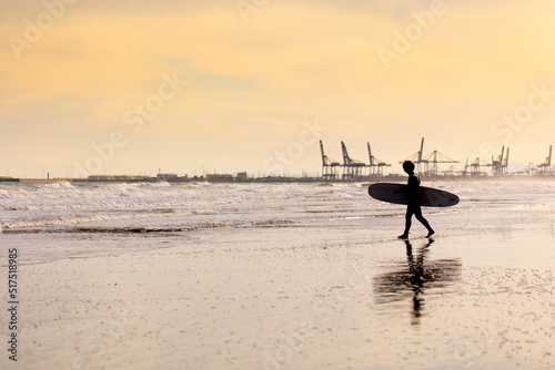 Summer atmosphere on the sunny autumn beach of Malvarrosa in Valencia, Spain. The sea coast attracts surfers for a leisurely ride on a board along the raging foamy waves. photo