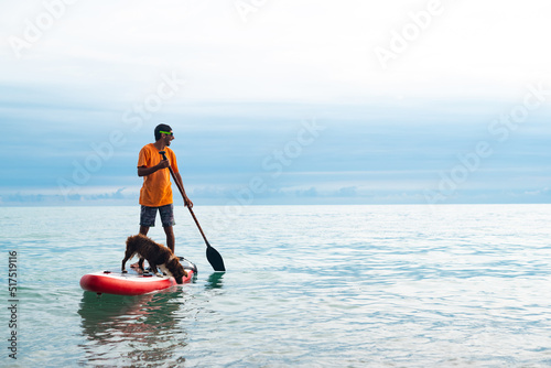 a guy on a sup board with a paddle with a dog stands on the sea in summer