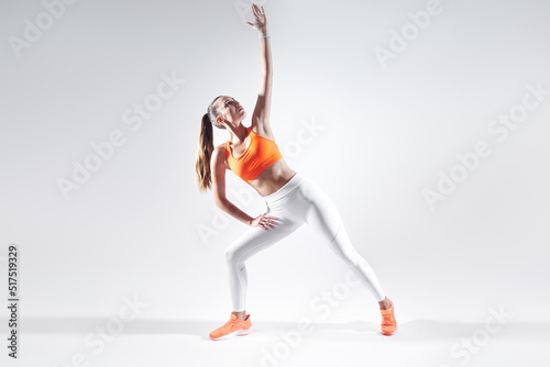 Beautiful young woman in sports clothing doing stretching exercises against white background