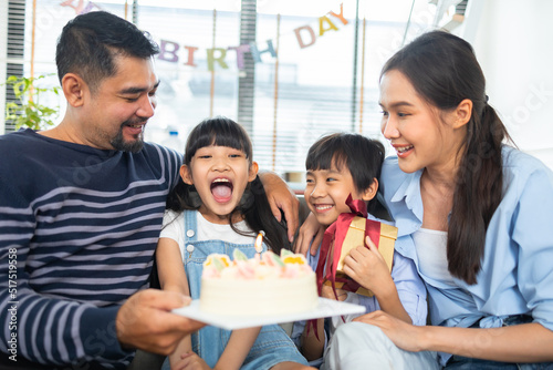 Asian family celebrating birthday together at home.Asian girl blow out candles on cake on table in happy birthday party and colors decorative items .