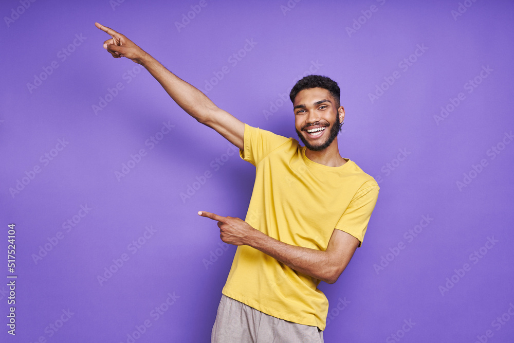 Handsome African man pointing away and smiling while standing against purple background Handsome African man pointing away and smiling while standing against purple background